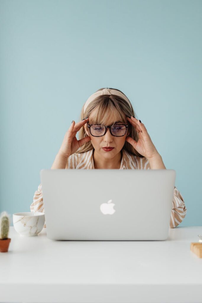 Woman in glasses working on a laptop, concentrating while seated indoors.